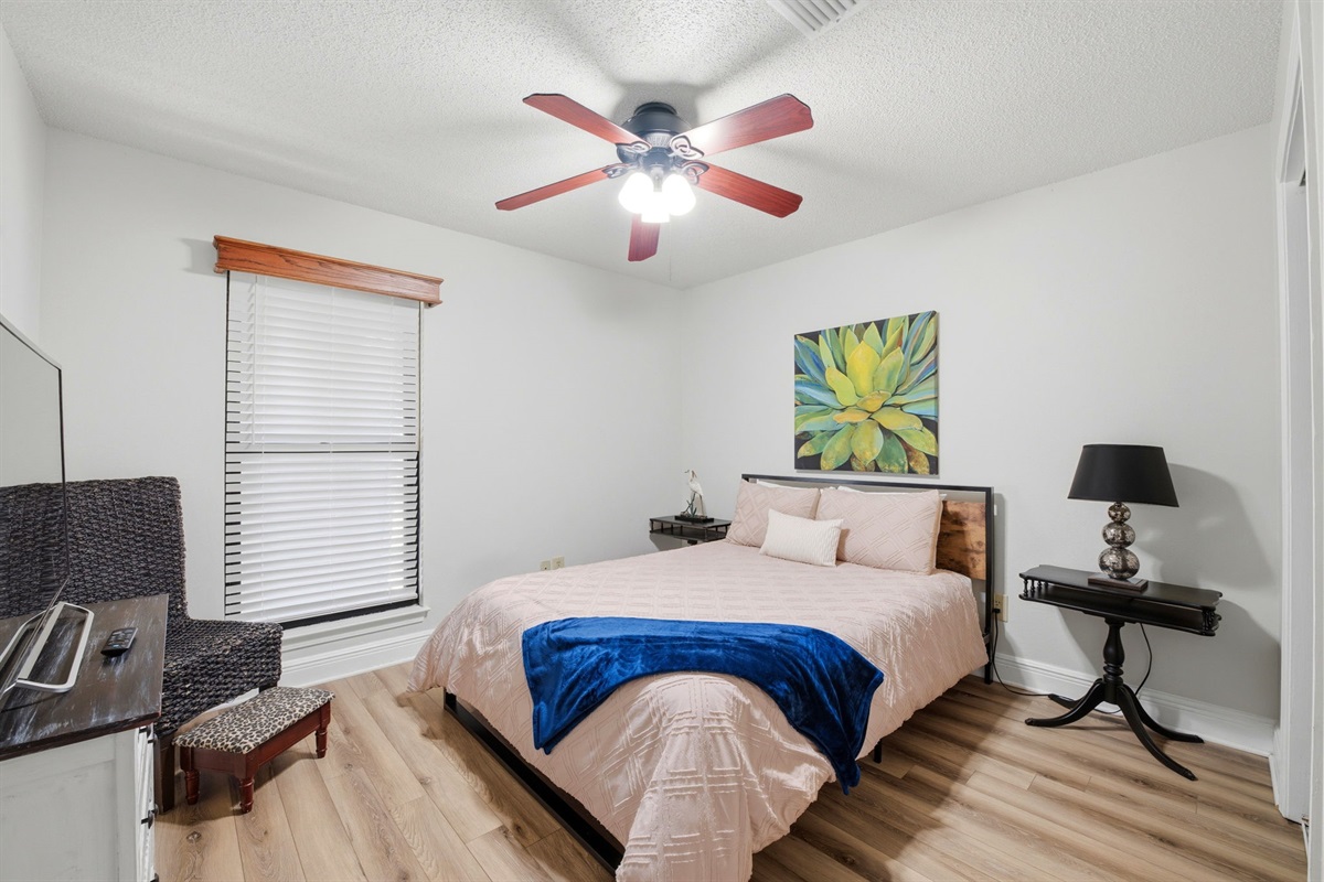 Bright and welcoming, this bedroom features a plush bed, ceiling fan, and stylish décor for a comfortable night’s rest. A TV and nearby seating area provide added convenience, making it a perfect space to relax and recharge.