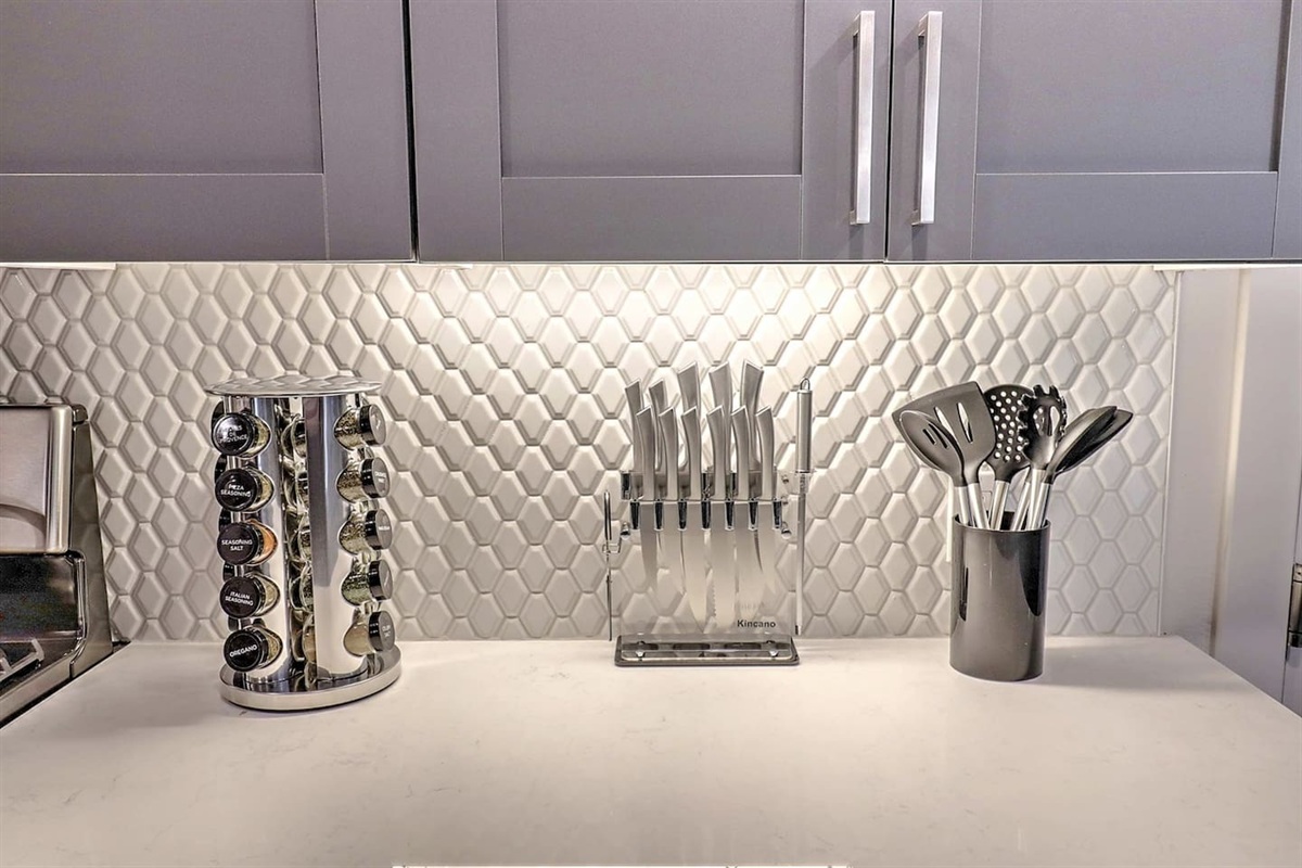 - Fully stocked kitchen setup featuring stainless utensils and sharp knife set   - Spice rack adds flavor variety for easy cooking and meal preparation   - Bright backsplash and sleek counters create a stylish cooking environment