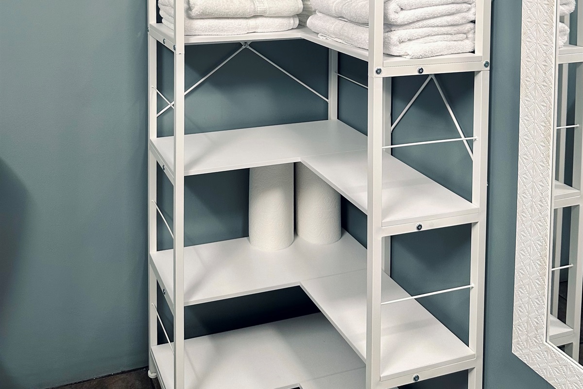 Basement bathroom shelving stocked with fresh bath towels, hand towels, washcloths, and makeup remover cloths. Includes cotton swabs, cotton balls, lotion, and generous additional storage—ideal for guests using the lower-level suite.