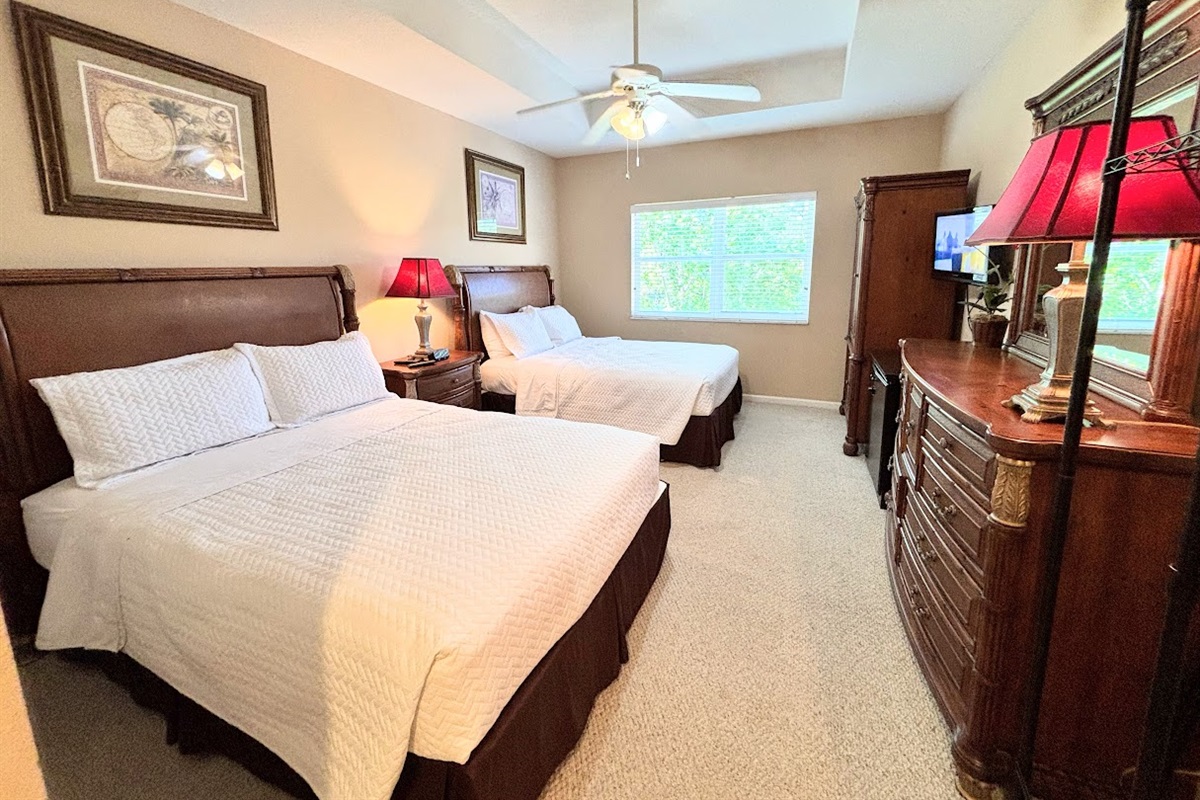 Comfortable bedroom featuring two beds, dresser storage, ceiling fan, TV, and plenty of natural light.