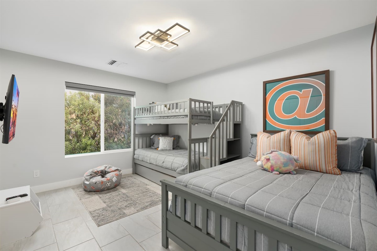 Fun kids' bedroom with bunk bed, single bed, and bold artwork for a playful vibe.
