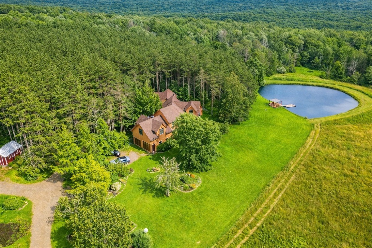 Stunning bird’s-eye view of the home nestled in trees, complete with a sparkling pond and open green fields.