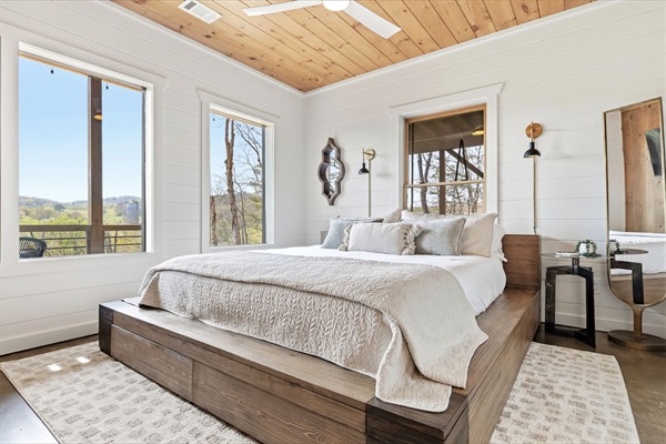 This bright and airy bedroom features a cloud like Serta mattress bed with storage drawers. Large windows fill the space with natural light and peaceful mountain views, while the warm wood ceilings and neutral tones create a calm, inviting retreat.