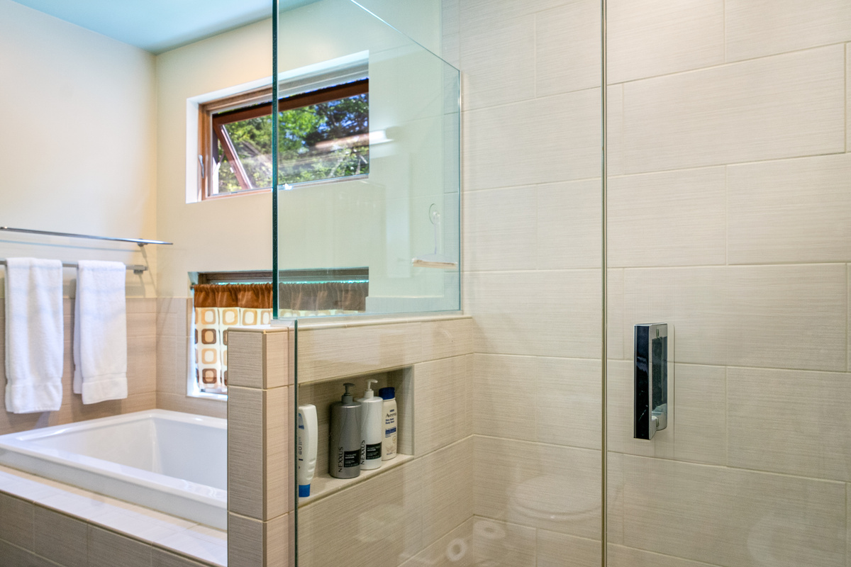 Spa-like primary ensuite featuring a deep soaking tub and a modern glass-enclosed shower. Bathed in natural light with the added comfort of a heat lamp, this private retreat is the perfect place to recharge after a day of Acadia exploration.