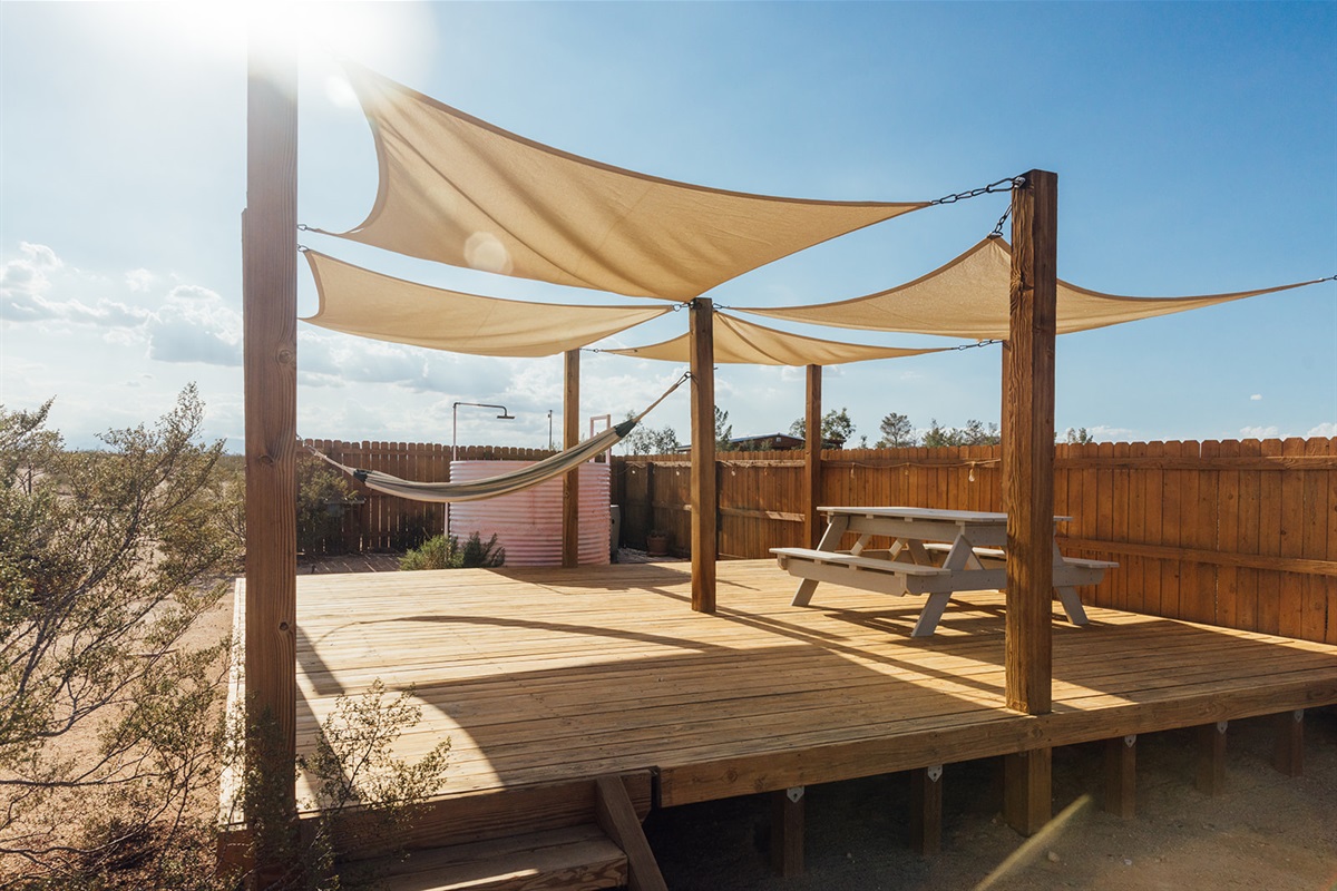 Spacious outdoor deck with hammock, picnic table, and shade sails overlooking the desert — an ideal space for dining, lounging, and stargazing.