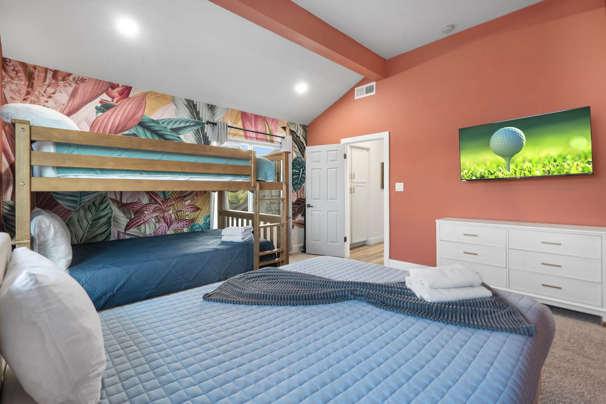 Colorful guest bedroom with queen bed, bunk beds, and vibrant botanical wallpaper.