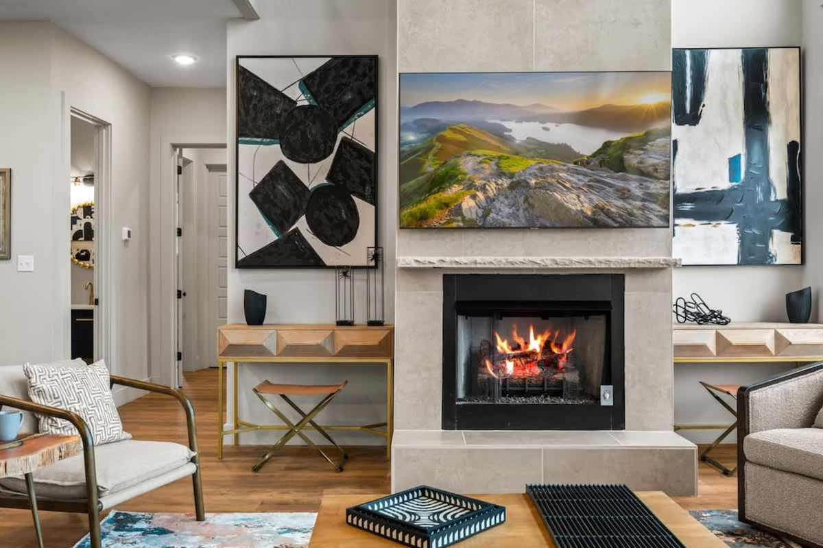 Gatlinburg cabin main living area with dramatic stone fireplace, panoramic mountain views, and natural light from floor-to-ceiling windows. Open staircase links all levels, creating a luxurious and welcoming Smoky Mountain retreat.