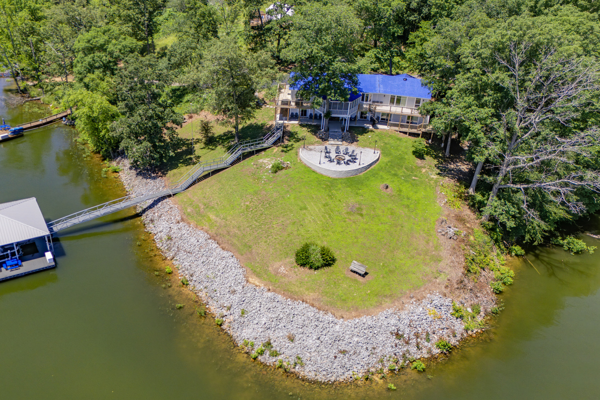 This overhead view shows the full lakefront layout, including the house, firepit area, lawn, shoreline, and dock.