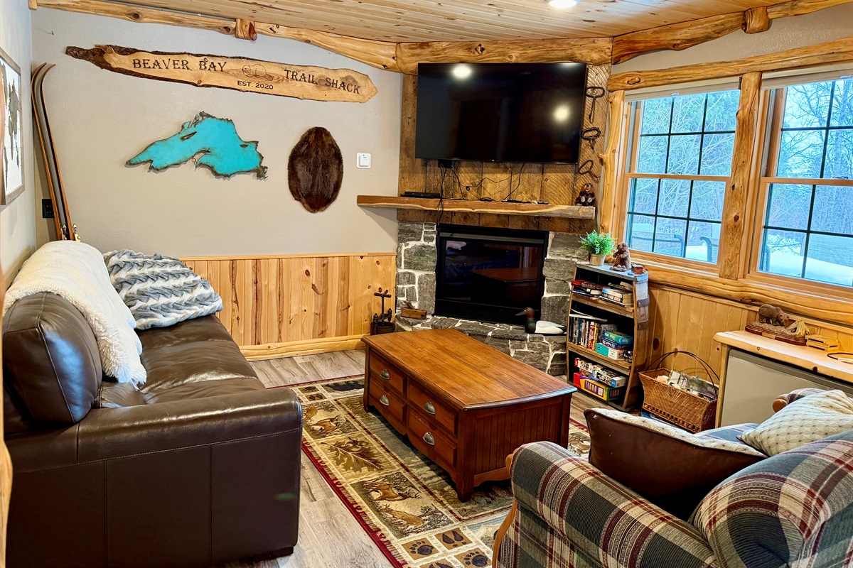 A cozy, inviting living room with plush couches, a fireplace topped by a TV, and large windows that bring in natural light. Thoughtful décor and a warm layout make it the perfect spot to relax after a day of adventure.