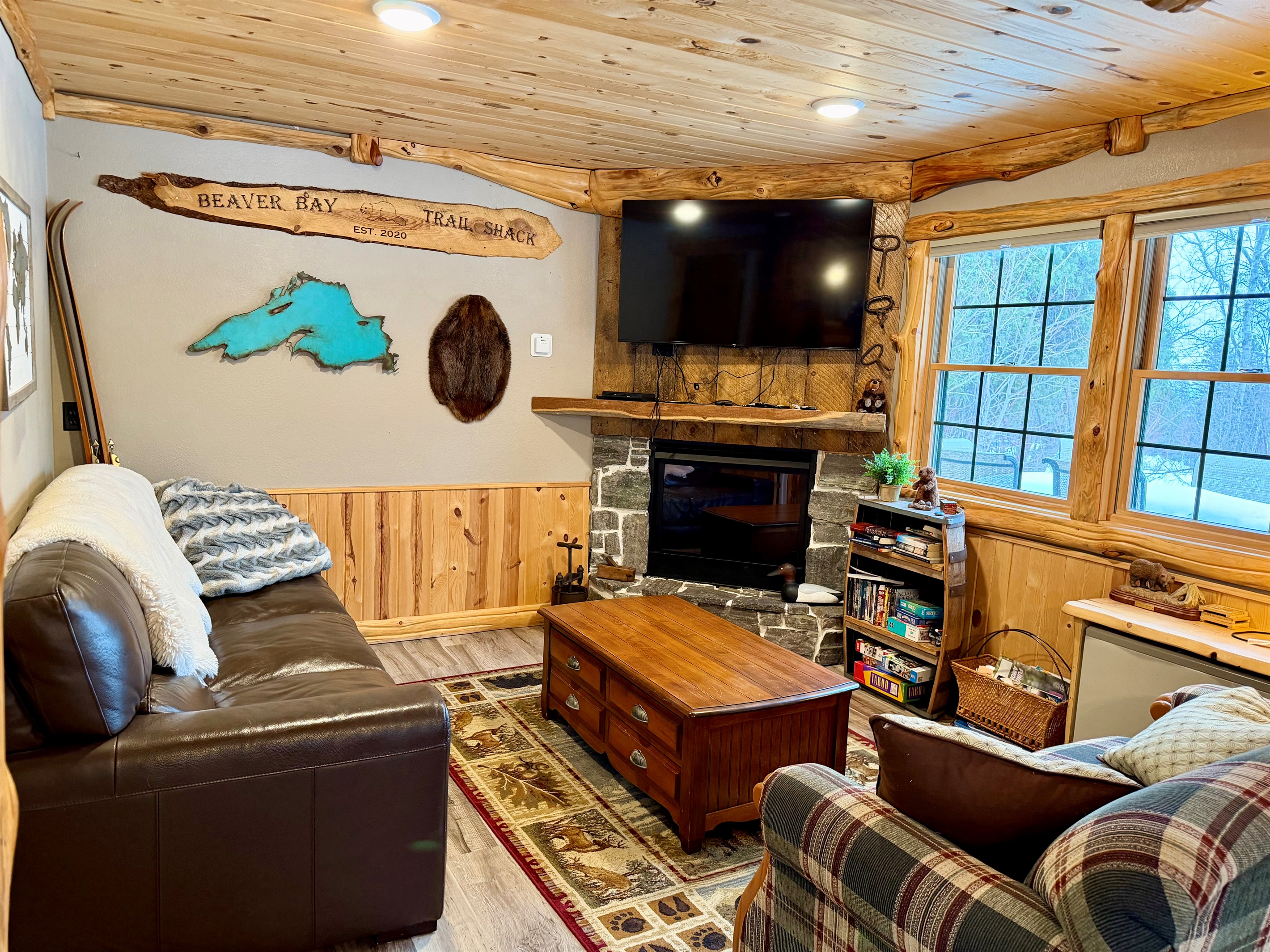 A cozy, inviting living room with plush couches, a fireplace topped by a TV, and large windows that bring in natural light. Thoughtful décor and a warm layout make it the perfect spot to relax after a day of adventure.