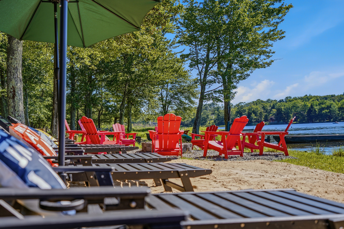 Waterfront lounge area with sun loungers, umbrellas, and red Adirondack chairs at the water's edge
