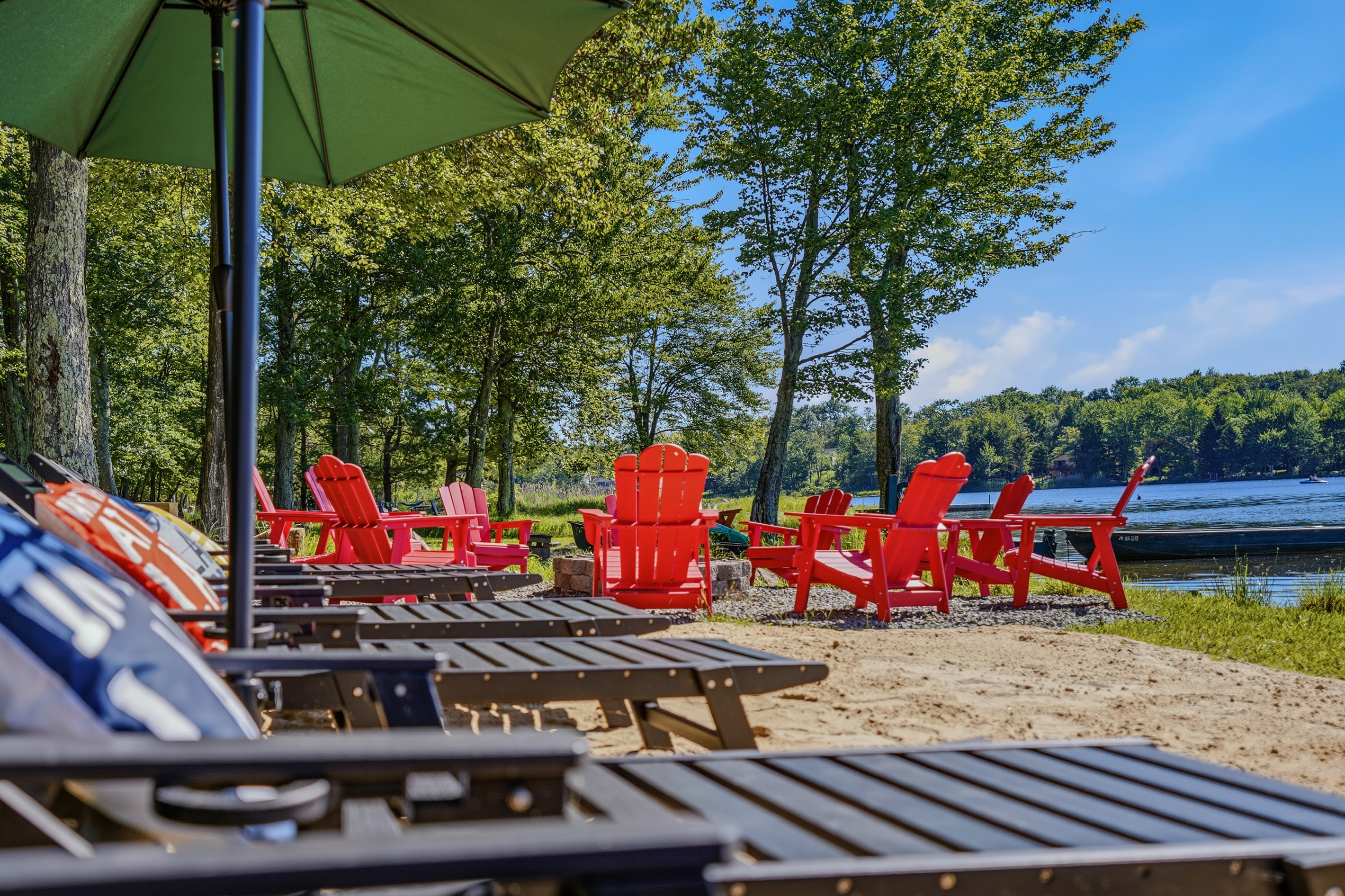 Waterfront lounge area with sun loungers, umbrellas, and red Adirondack chairs at the water's edge