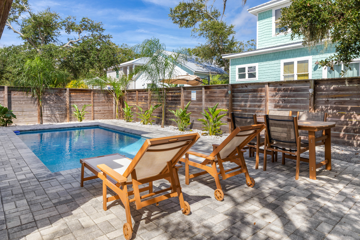 The pool sits behind a full privacy fence with young palms filling in all around it. Two loungers, a high-top table for cards, and water that stays heated - which is what stretches the swimming well past summer.