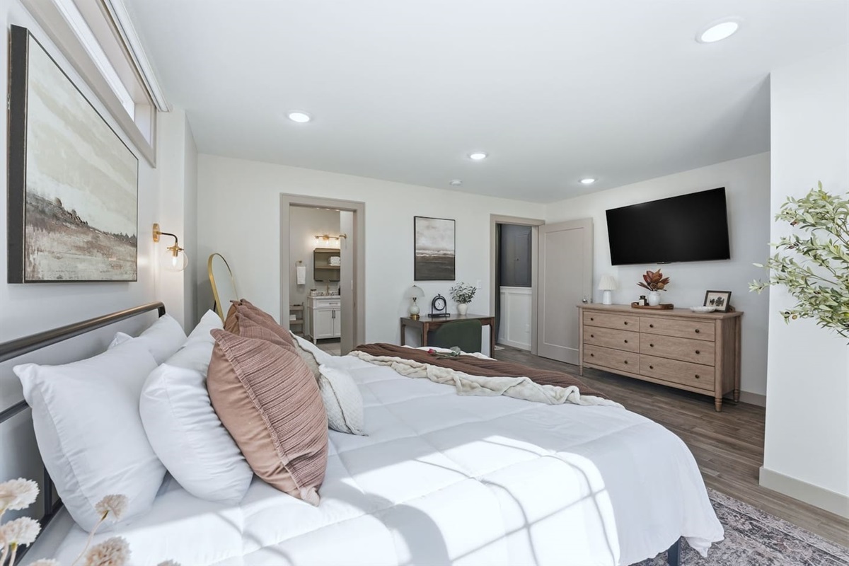 Another view of the serene bedroom with a plush king bed, wall-mounted smart TV, dresser storage, and a dedicated workspace.