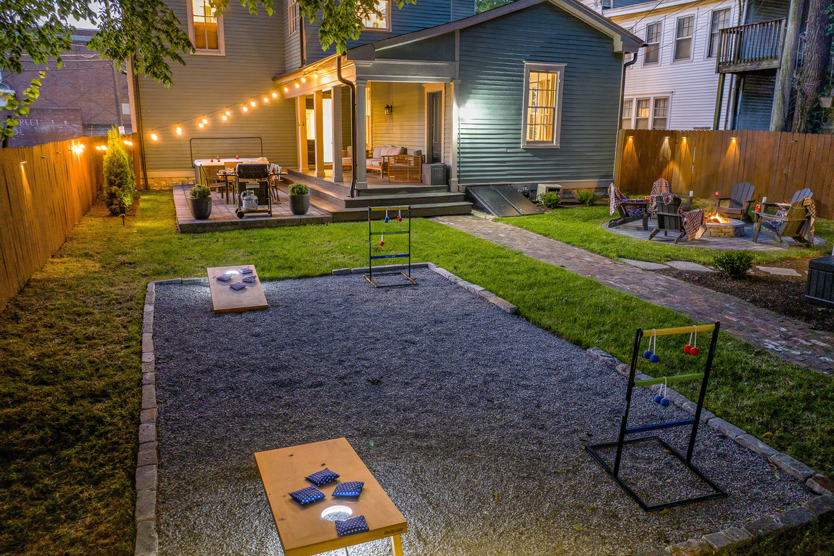 The full backyard at dusk: fire pit lit, game room glowing, covered porch set and ready.
