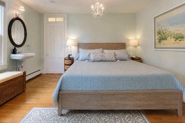 The second king bedroom on the second floor — a crystal chandelier, hardwood floors, and a palette that feels exactly right for a Cape May summer.