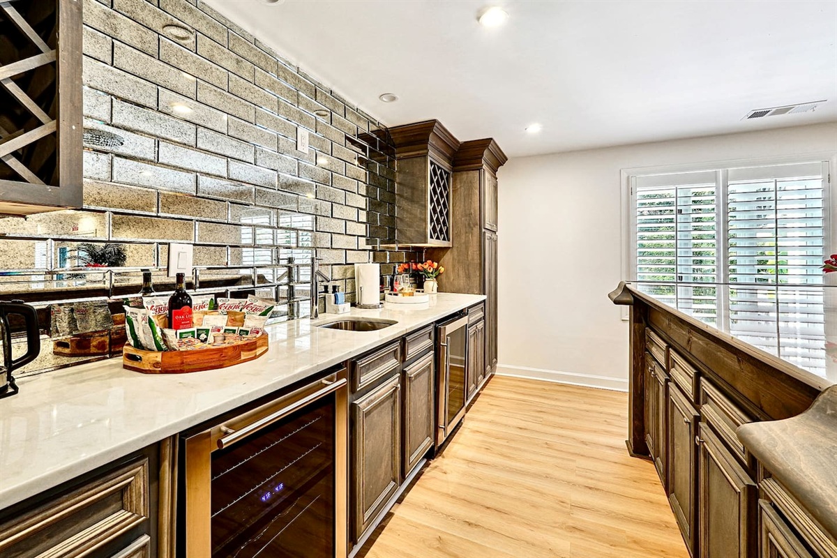 Basement kitchenette located to the left at the bottom of the stairs, featuring a sleek bar with seating, sink, two coolers, wine cabinetry, and modern gray cabinets with a matching backsplash, convenient as it is right next to the game room!
