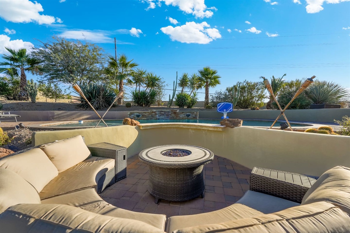 Cozy circular fire pit seating overlooking the pool, surrounded by desert landscaping and palm trees.