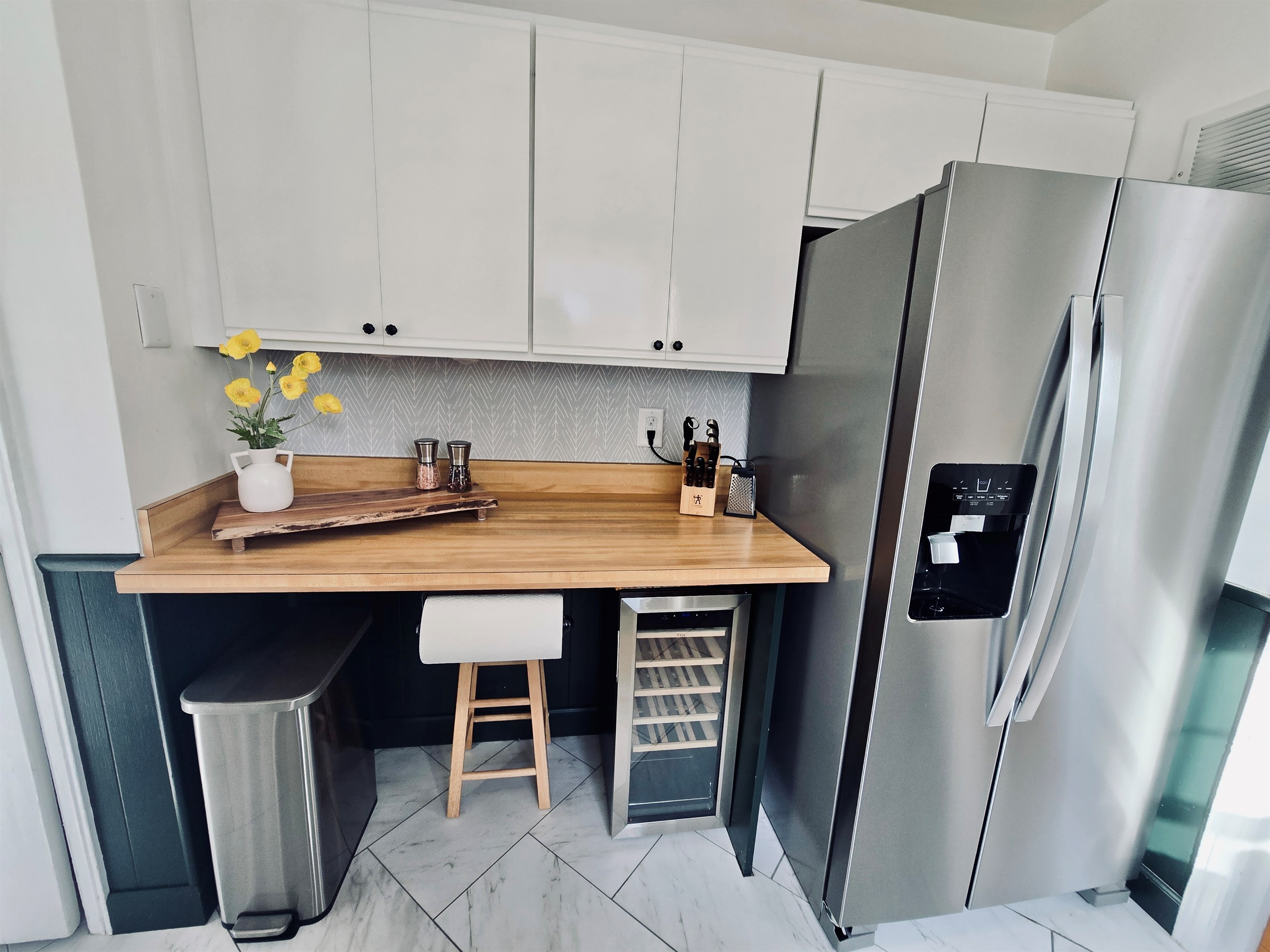Kitchen comforts meet everyday ease: stainless steel fridge, wine cooler, and a curated countertop lineup—knives, grinders, and a stool that’s perfect for sipping coffee or keeping the cook company.