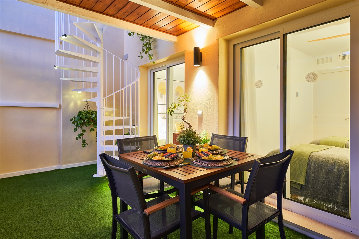 Private covered balcony with dining area, lush plants, and ambient lighting — ideal for a relaxed breakfast or a cozy evening meal.
