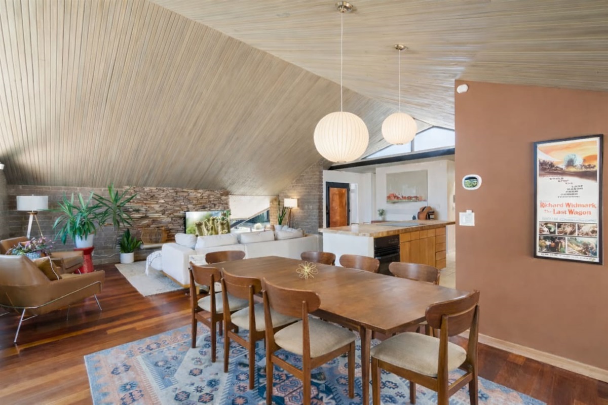 Inviting living and dining area with statement lighting, exposed stone wall, and cozy mid-century design details.