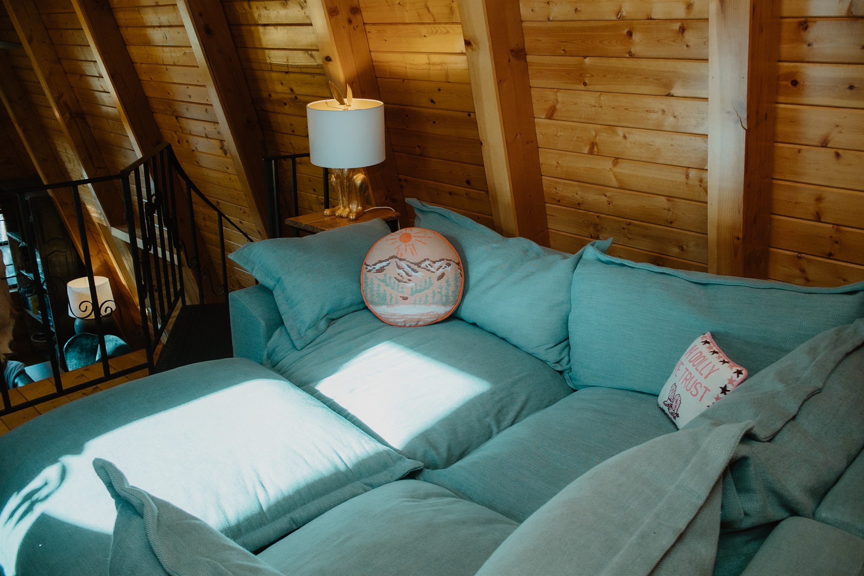 Sunlit loft lounge with vaulted A-frame ceilings, plush seating, and warm wood beams. This cozy mountain cabin offers the perfect spot to unwind, read, or relax while overlooking the living space below.
