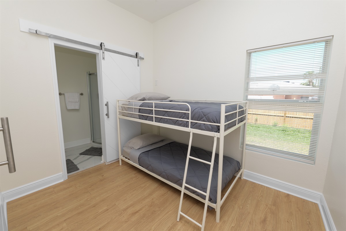 This bright bedroom features sleek metal bunk beds, soft linens, and a sliding barn door that opens to a private bath.