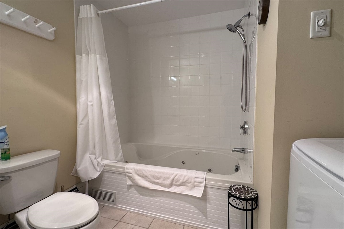 The bathroom has a large jetted tub and shower and a washer and dryer behind the door. 