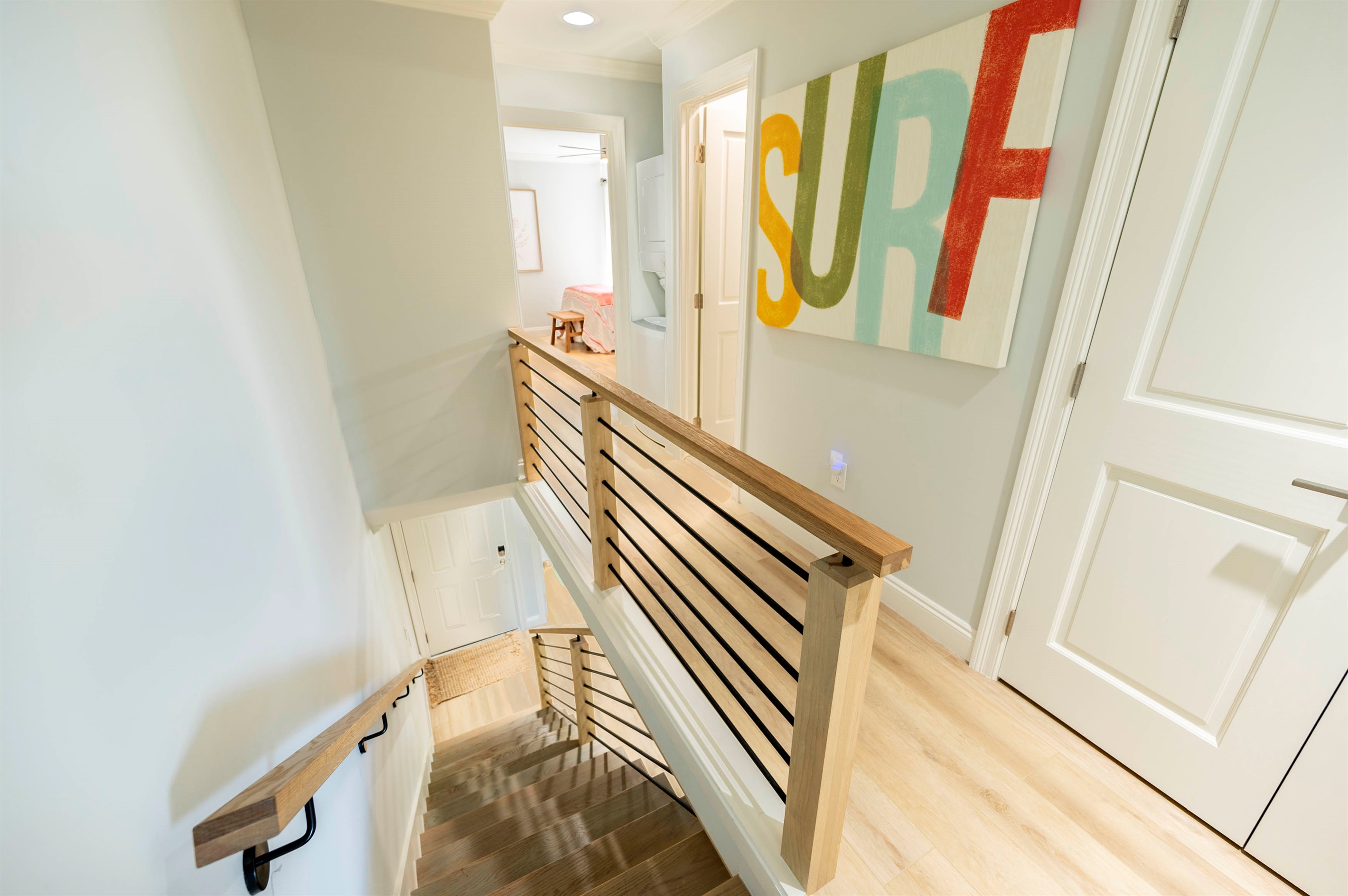 Bright staircase charm with sleek wood railings and colorful 'SURF' wall art.