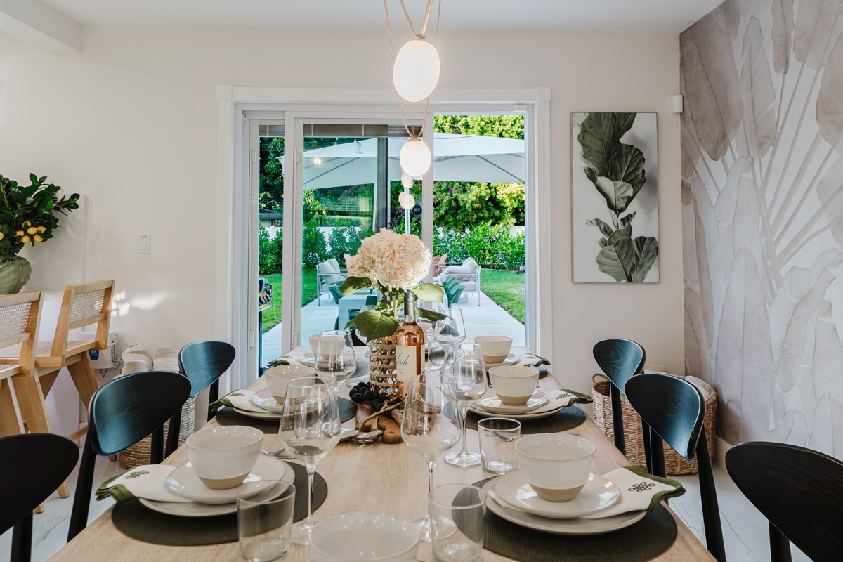 Designer dining room featuring a Gwyneth Paltrow GOOP statement light, custom wallpaper, and seating for 12. Backlit counter seating and seamless access to the patio and backyard make this space ideal for family meals and entertaining.