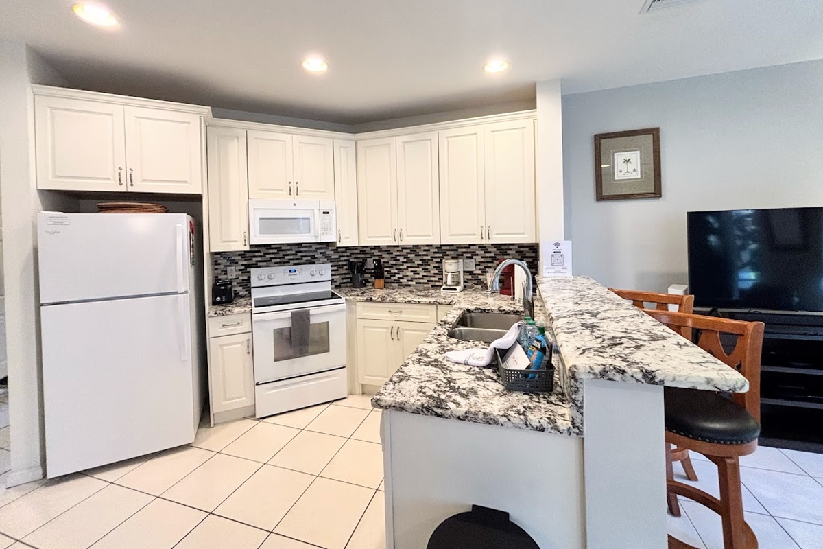 Updated kitchen featuring granite countertops, full-size appliances, breakfast bar seating, and an open view into the living area.