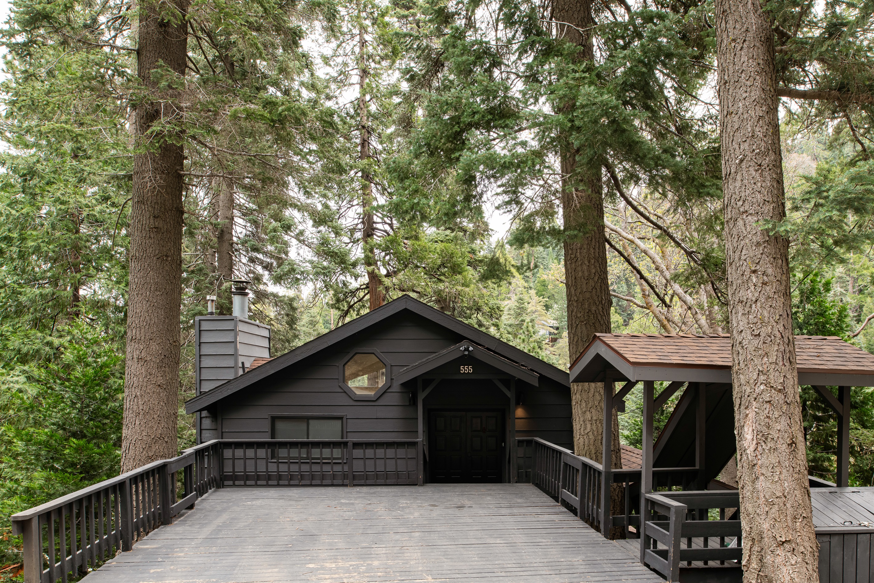 Welcoming cabin exterior with 2-Car Driveway Deck, surrounded by tall pines—your private mountain escape starts right at the front door.