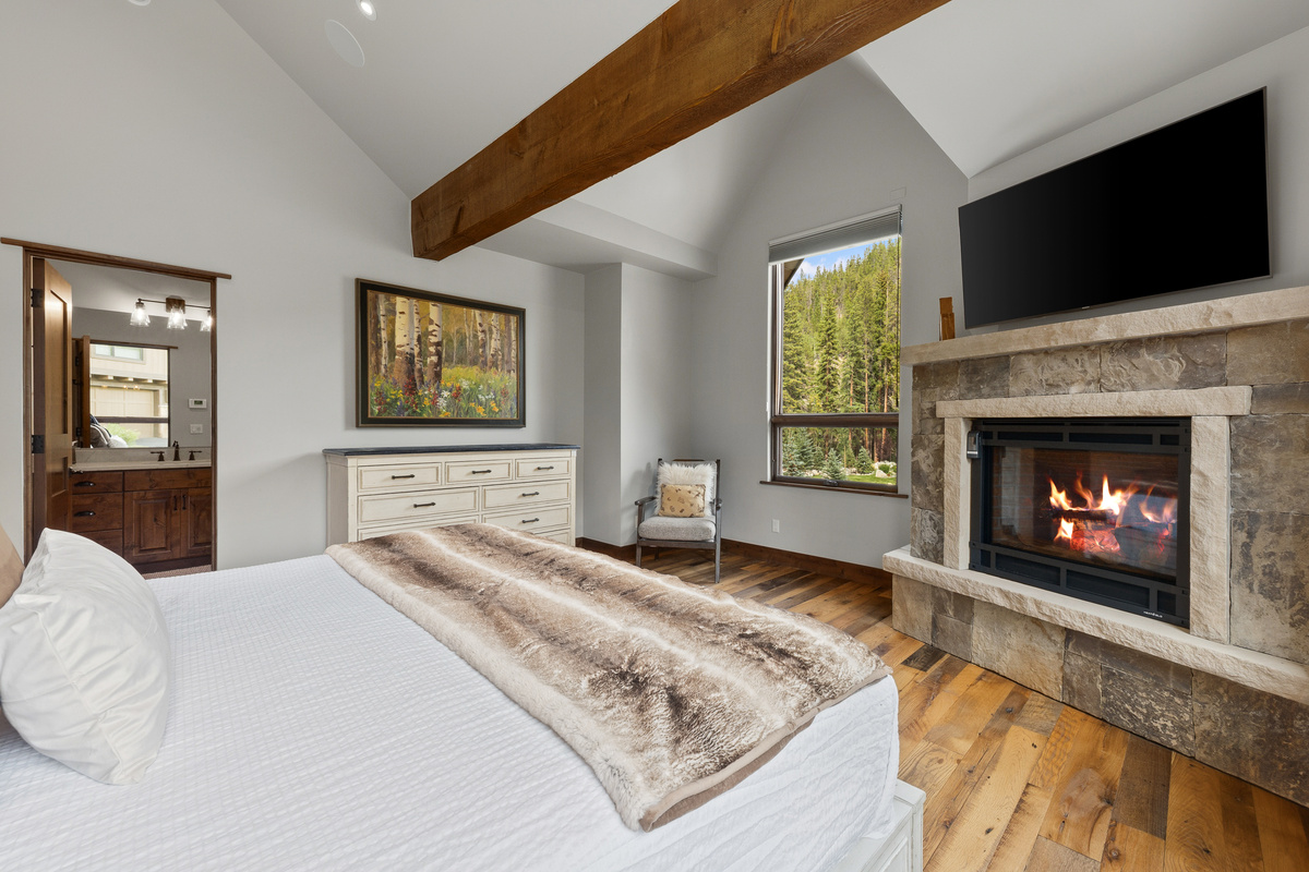 Primary bedroom with King bed, gas fireplace, vaulted ceilings, numerous windows, and en-suite full bathroom. 