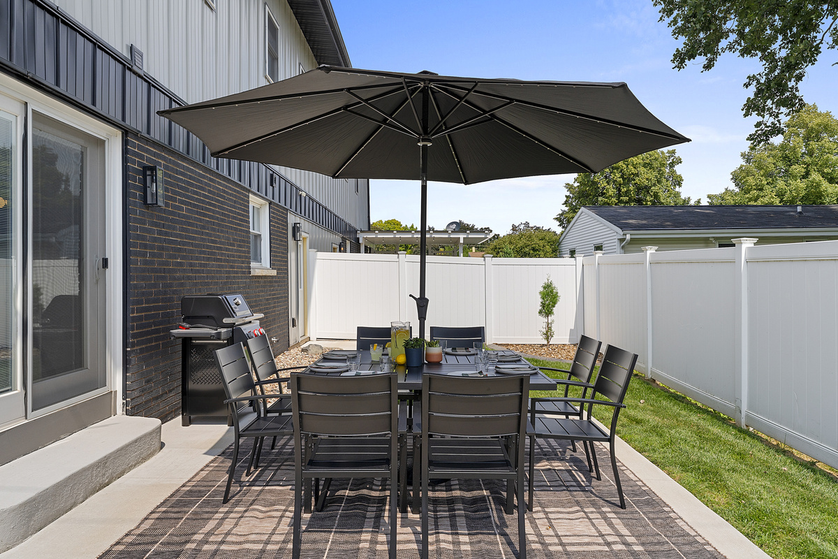 Outdoor dining for eight with a Weber gas grill and partially fenced yard.