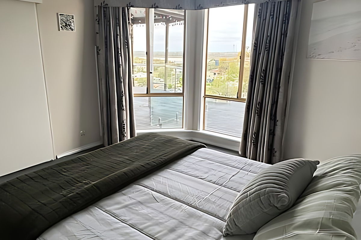 The queen bed in Bedroom 1 faces a bay window looking out past the deck to Preston Beach and Lake Preston, giving the main bedroom of this single-level home a lake outlook.