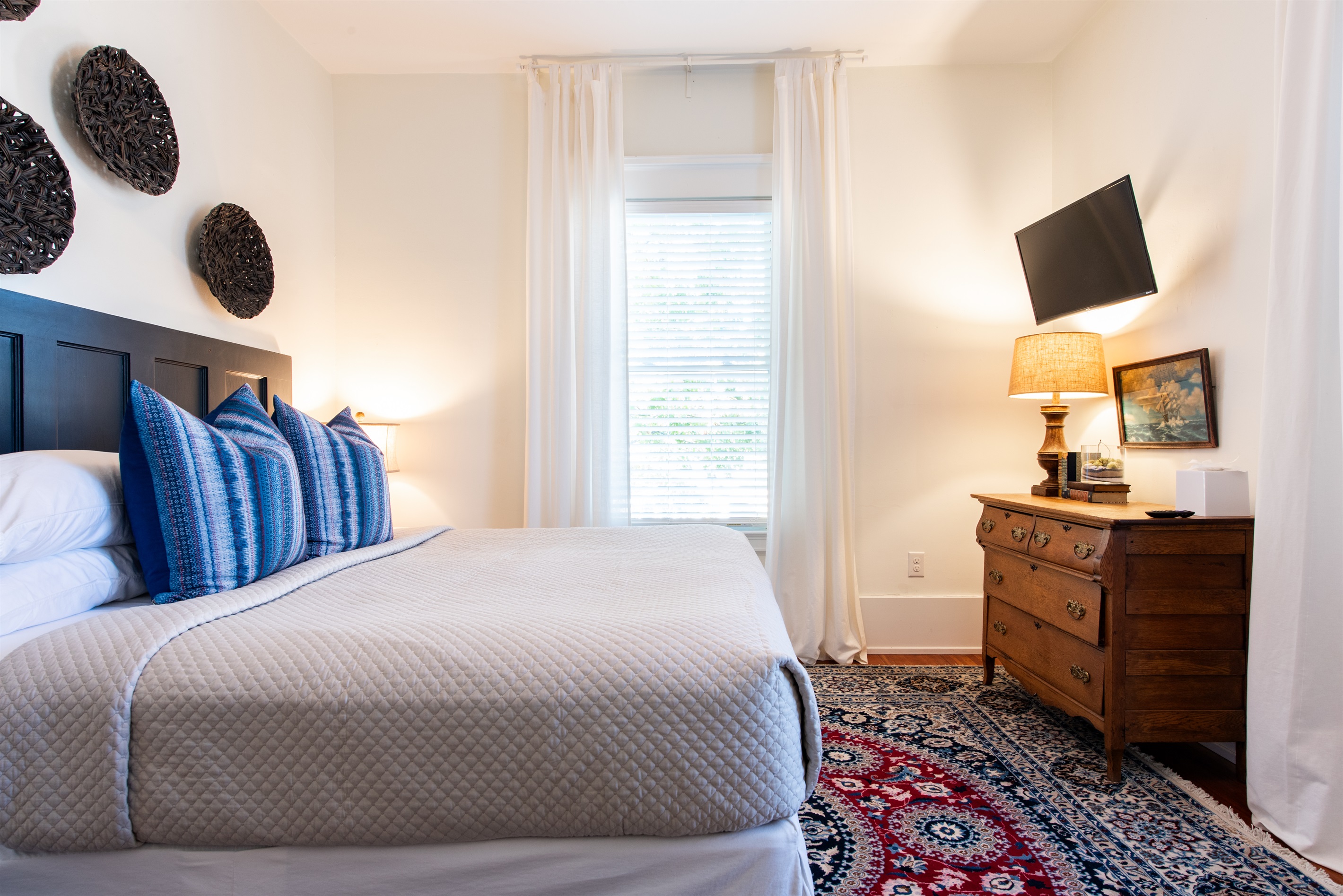 Unwind in this elegant bedroom on the Bourbon Trail in Louisville’s Highlands! Featuring a plush bed with blue pillows, a vintage dresser, a TV, & woven wall art—perfect for a restful stay!