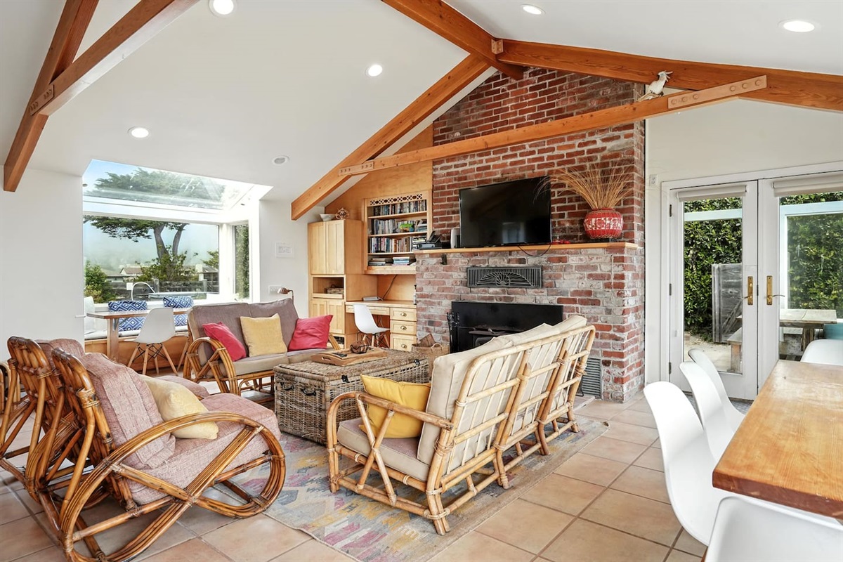 - Spacious open living area with multiple seating zones and large dining table  
- Brick fireplace and exposed beams enhance the cozy yet airy design  
- Walls of windows showcase stunning outdoor views from every angle  