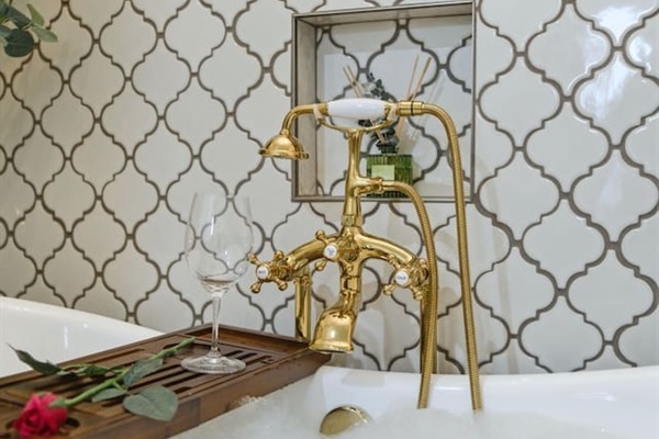 Luxurious soaking tub with elegant gold fixtures, perfect for unwinding with a glass of wine 
