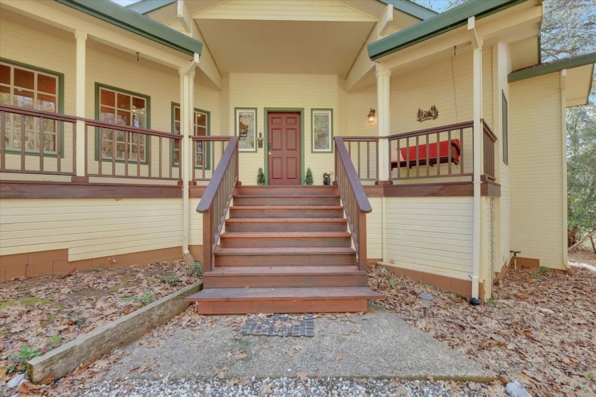 Front porch entry with steps, covered seating, and a quiet wooded setting around the home.
