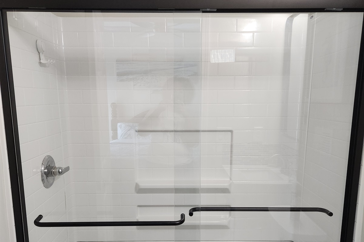 Step into this spacious walk-in shower enclosed in sleek glass doors and surrounded by clean white tile.