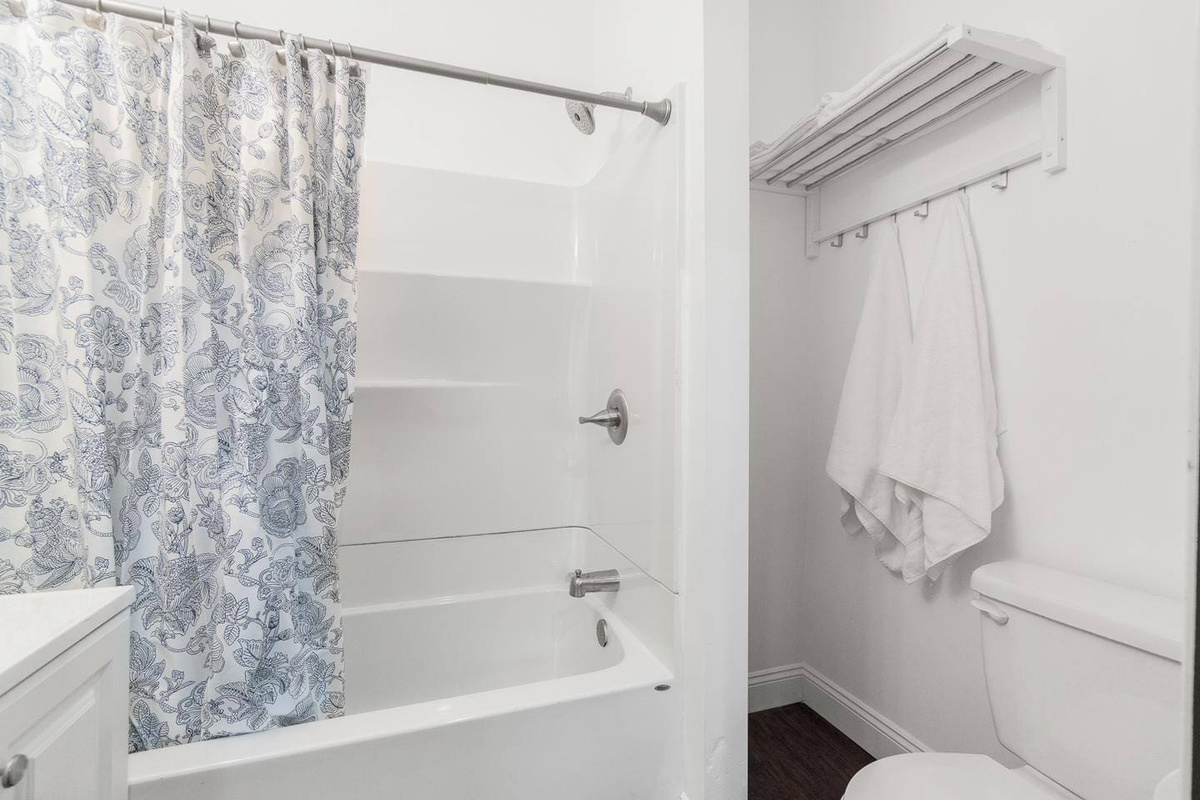 Modern bathroom equipped with a tub, toilet, mirror, and soft towels. Stocked with essentials like soap, shampoo, conditioner, and toilet paper, it has everything you need for a refreshing experience.