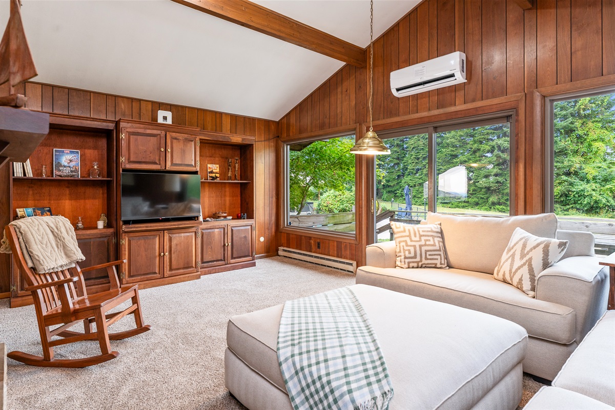 Relax in the bright, airy living room featuring plush seating, sliding doors to the deck, and scenic views of the surrounding greenery.