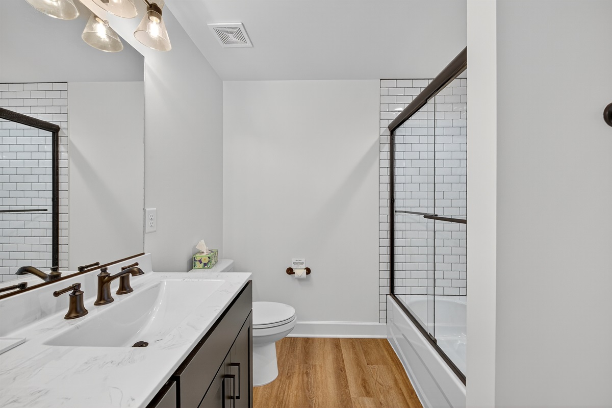 Impeccably designed full bath with a spacious double vanity, warm wood-grain flooring, and a classic subway-tiled shower/tub combination.