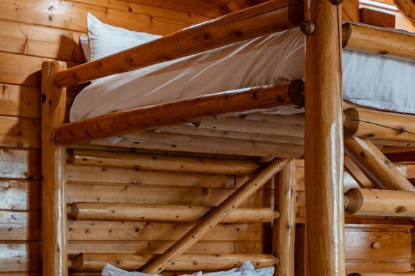 Lower level queen-over-queen log bunk — sleeps four, fresh linens, right in the heart of the game room so nobody misses a minute of the action.