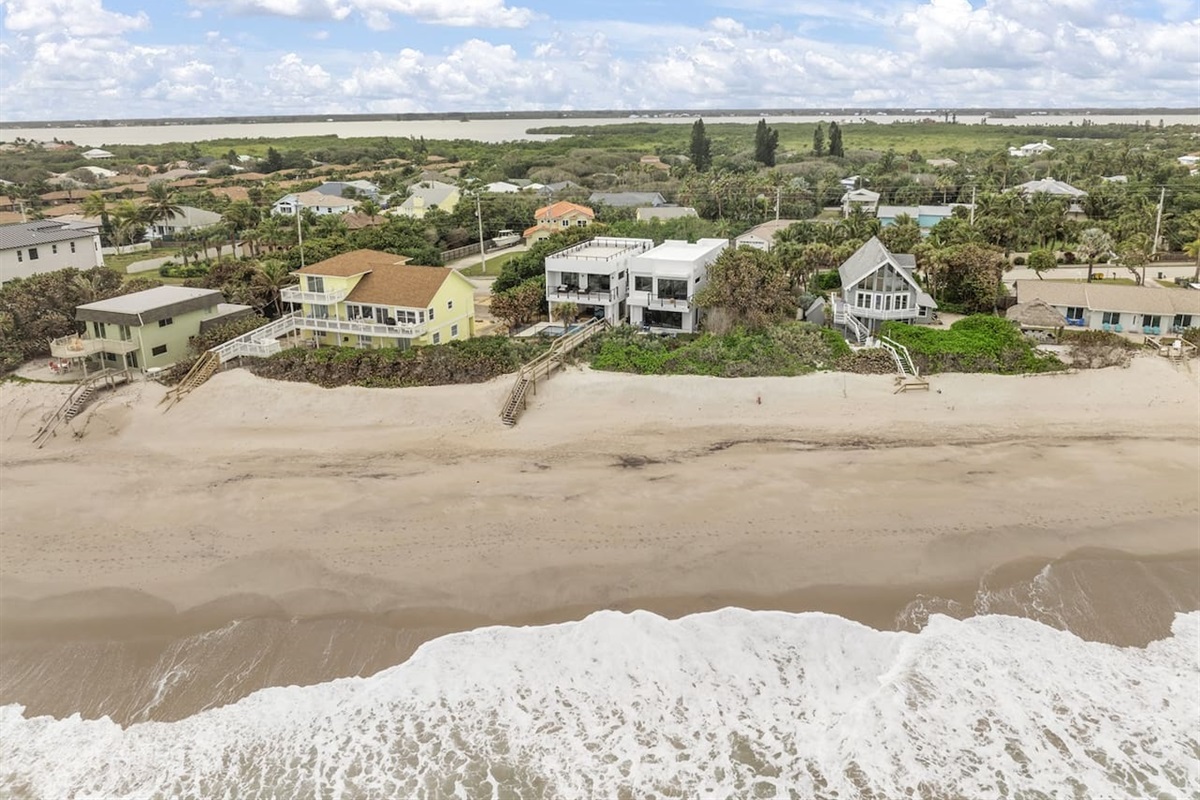 This breathtaking backyard showcases the neighborhood, vibrant trees, the shimmering sea, soft white sand, and fluffy white clouds, offering a perfect blend of coastal beauty and natural serenity.