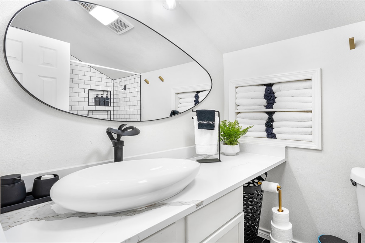 Step into this modern bathroom oasis, complete with a chic oval mirror and sleek vessel sink. The elegant white subway tiles and plush towels create a refreshing and calming space, perfect for getting ready or unwinding after a long day.