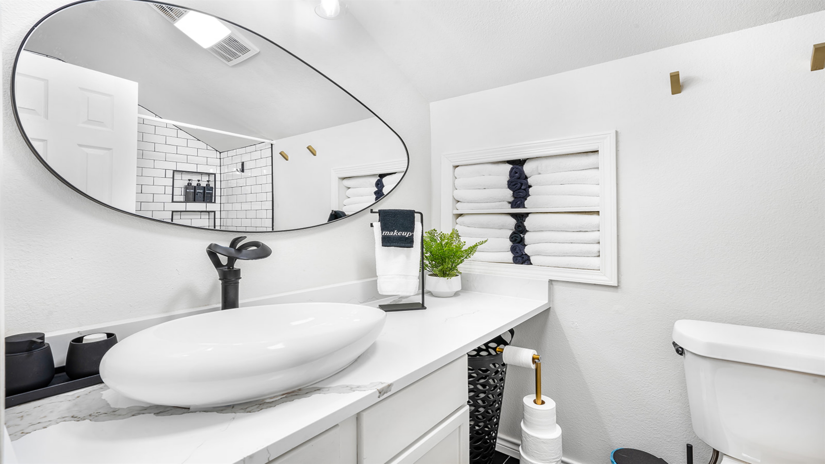 Step into this modern bathroom oasis, complete with a chic oval mirror and sleek vessel sink. The elegant white subway tiles and plush towels create a refreshing and calming space, perfect for getting ready or unwinding after a long day.