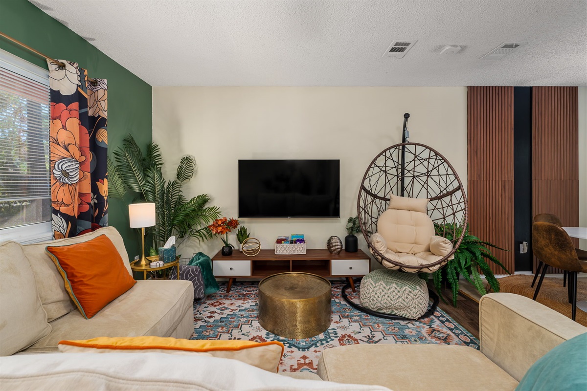 The cozy living room with a 55" smart TV, plush sectional couch, and cozy hammock chair.