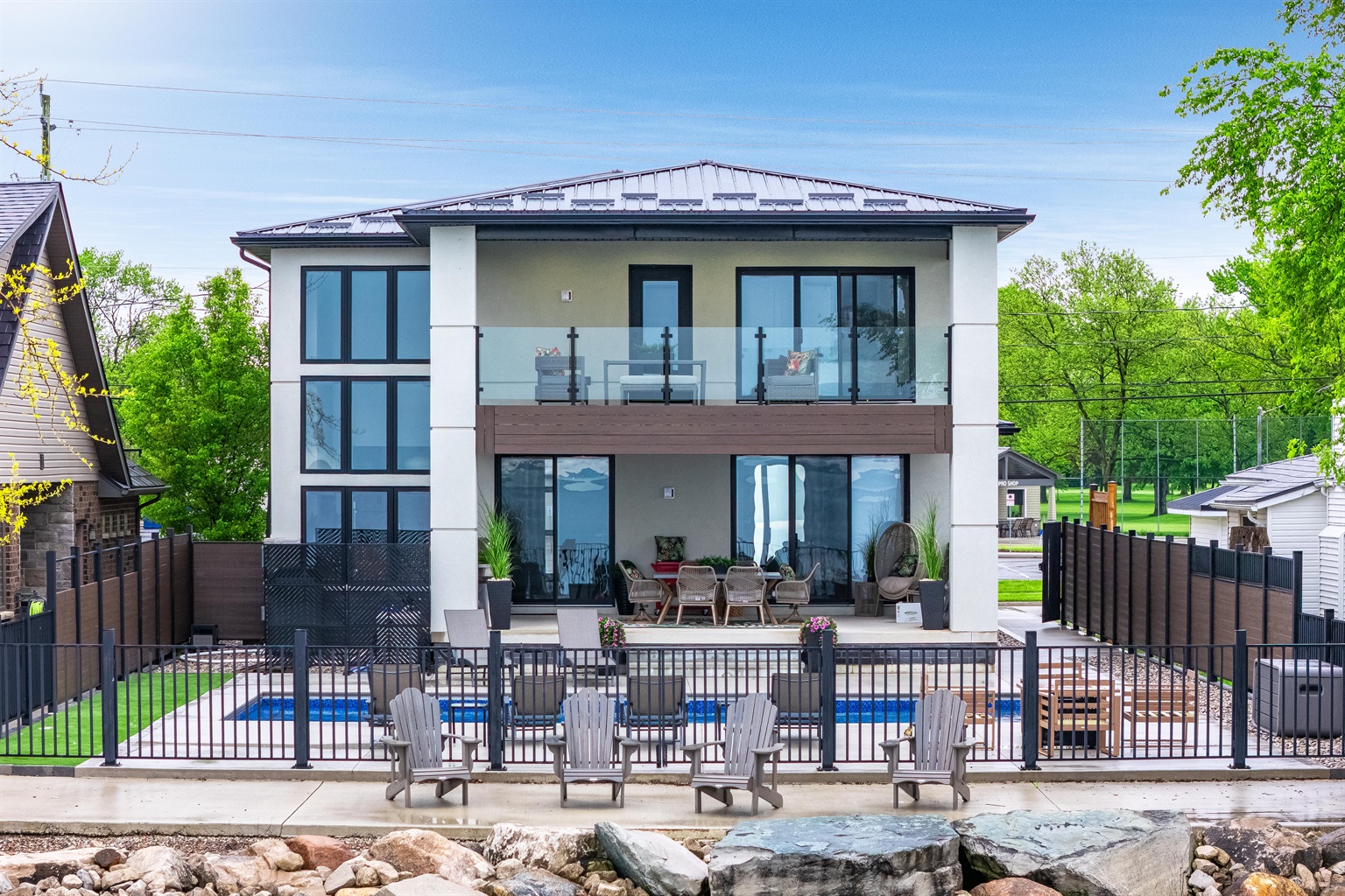 Backyard amenities include a paved water's edge deck, saltwater pool with sun loungers, a covered outdoor kitchen and dining area, and second story balcony with a comfortable outdoor lounge set with stunning lake views.