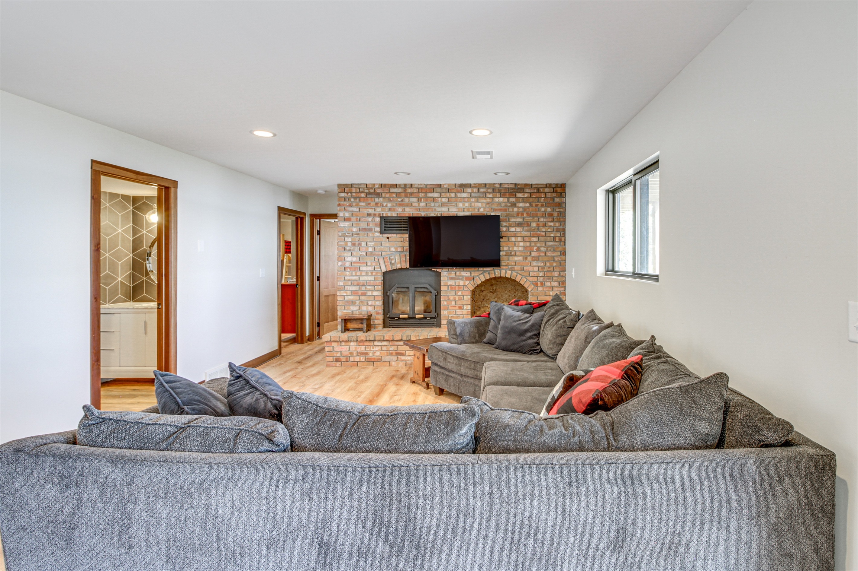 Lower-level family room with large sectional, smart TV, and cozy brick fireplace